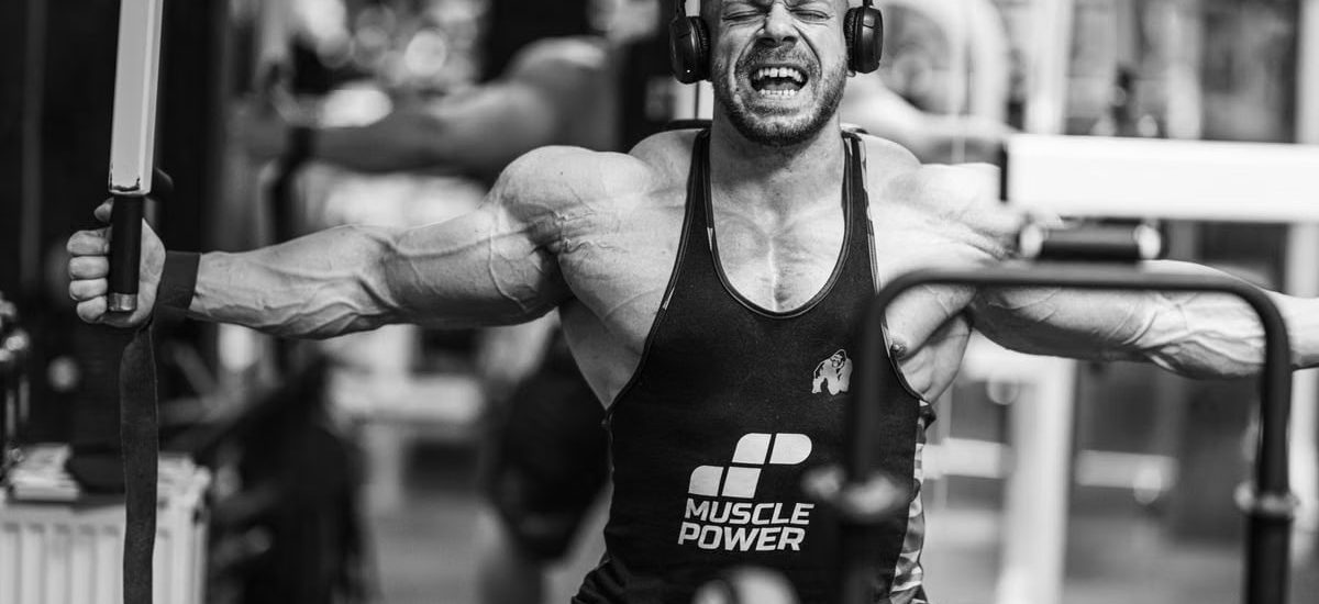 Muscular man intensely working out with gym equipment, showcasing strength and focus.