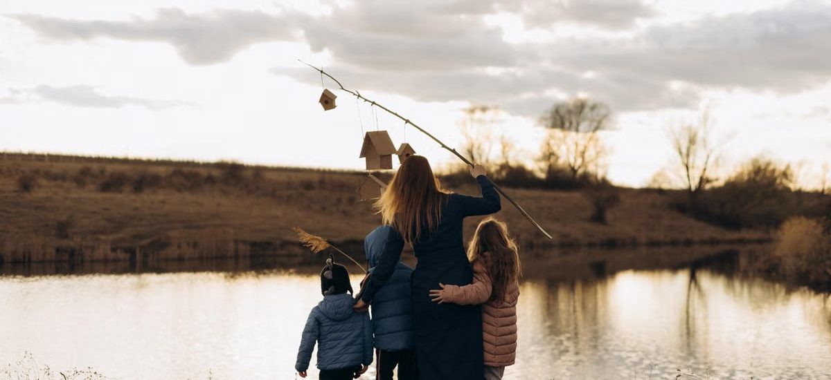 Family enjoying quality time by the lake at sunset with birdhouses.